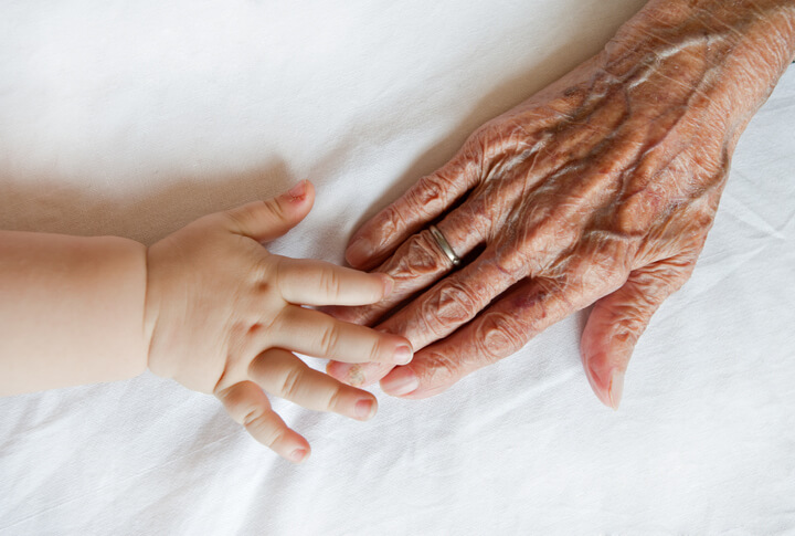 An infant and an elderly community support worker holding hands.