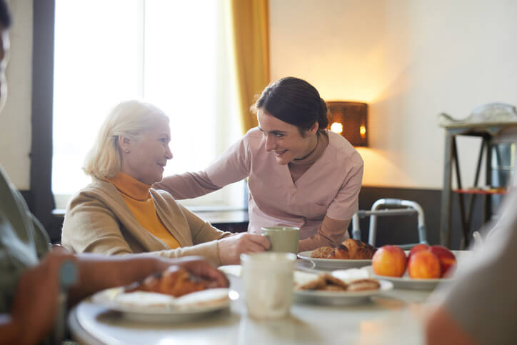 A health care assistant comforting clients as they eat at the table.