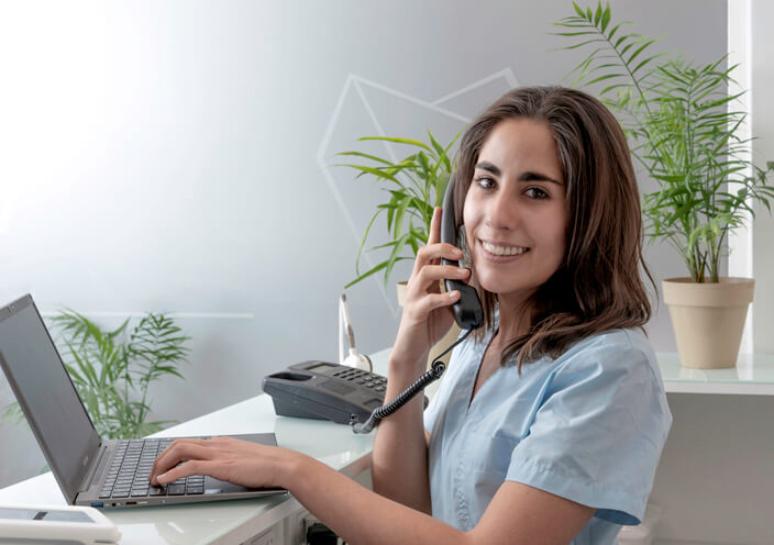 A dental reception training grad taking a phone call at the front desk of a dental office.