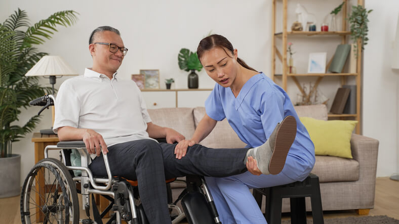 A health care assistant training grad helping a senior client with rehabilitation exercises from his wheelchair.