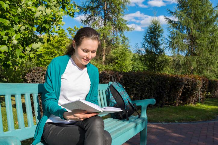 A female mental health worker sitting in the park reading a book to destress.