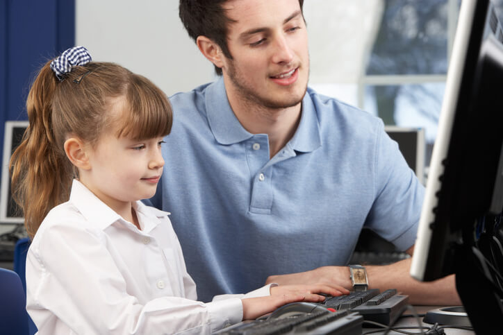 A male education assistant showing a student how to use a computer after his education assistant training
