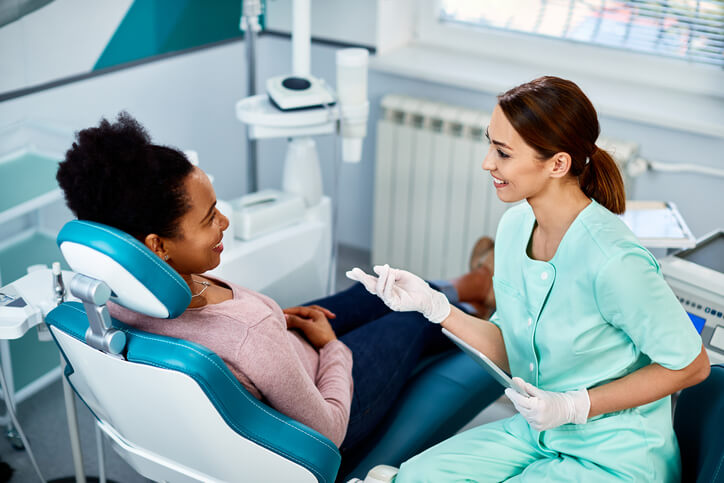 A smiling female dental assistant talking with a smiling patient about good oral hygiene after her dental assistant training