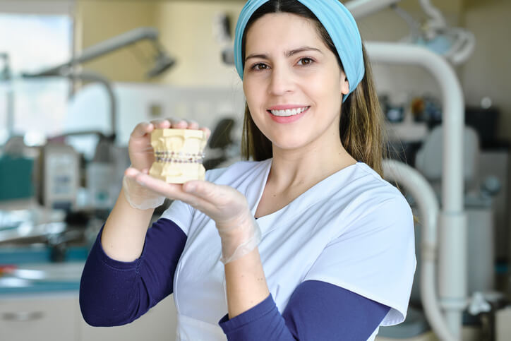 A smiling female dental assistant holding a dental prosthesis after completing her dental assistant training
