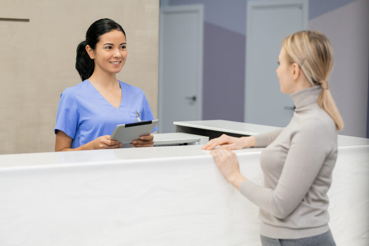 A smiling female medical office assistant interacting with a patient after completing her medical office assistant training