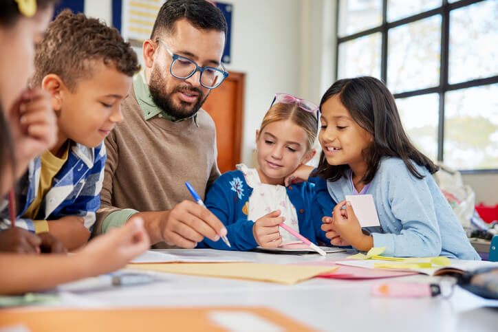 A male education assistant checking pupils’ homework in a classroom after completing his education assistant training