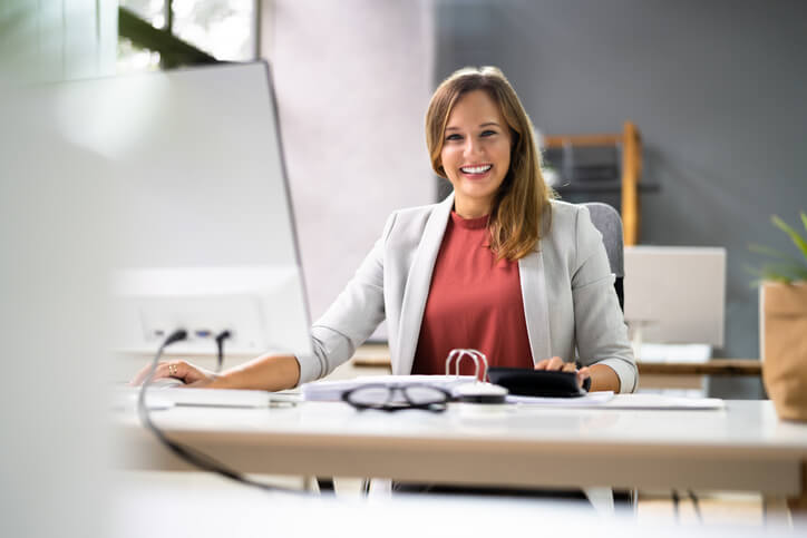 A smiling female records administrator accessing patients’ electronic health records in an office at the hospital after completing her medical office administrator training