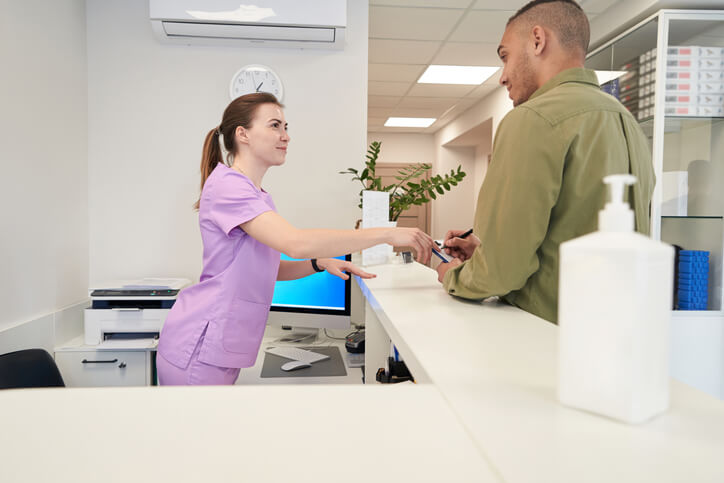 A female records administrator helping a male patient fill out a patient form in a hospital after completing her medical office administrator training