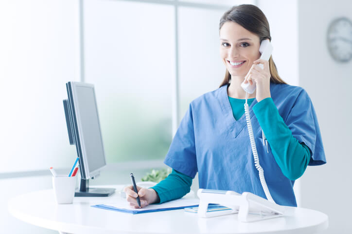 A healthcare training grad speaking on the phone at a clinic front desk