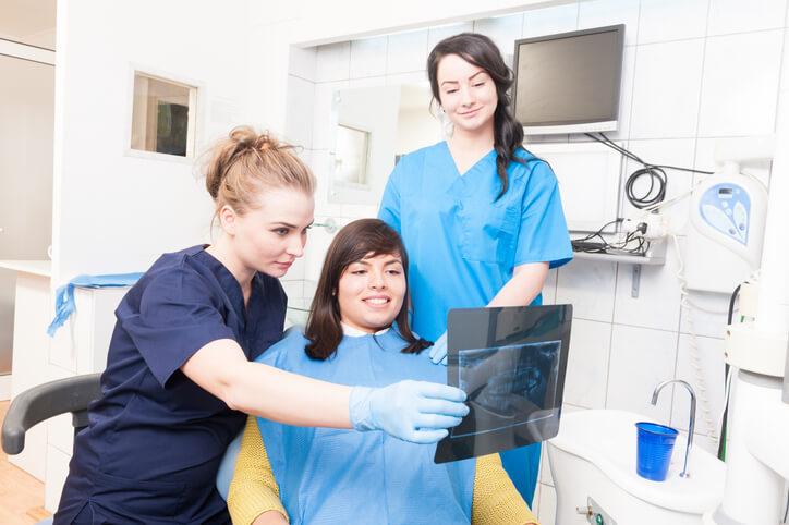 A dental assistant diploma graduate assisting a dentist with X-ray imaging