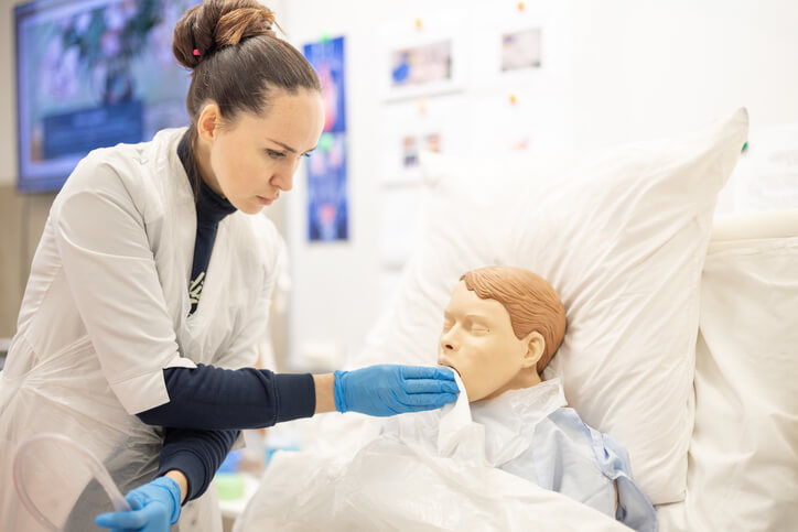 A health care assistant student practicing with a patient mannequin