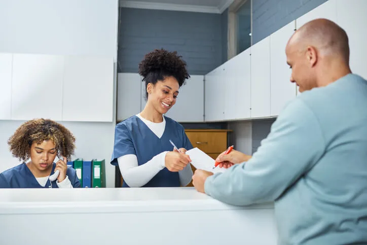 A dental receptionist in BC assists a patient at the front desk, demonstrating strong communication and customer service skills.