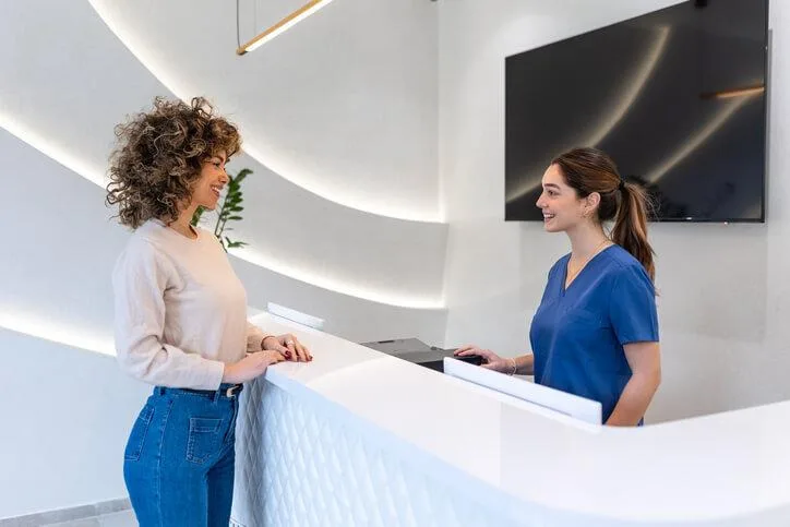 A dental receptionist assists a patient at the front desk of a dental clinic.